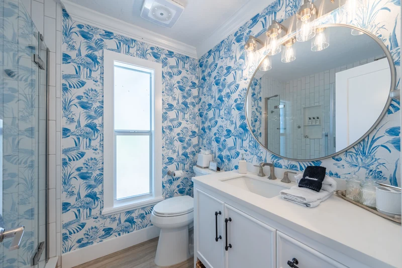 Bathroom with blue botanical wallpaper, a round mirror and folded towels